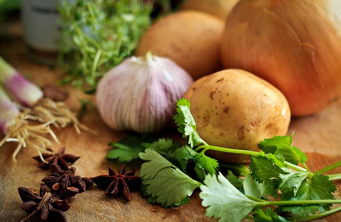 Aardappelen, knoflook, peterselie, bosui, steranijs en uien op een houten snijplank